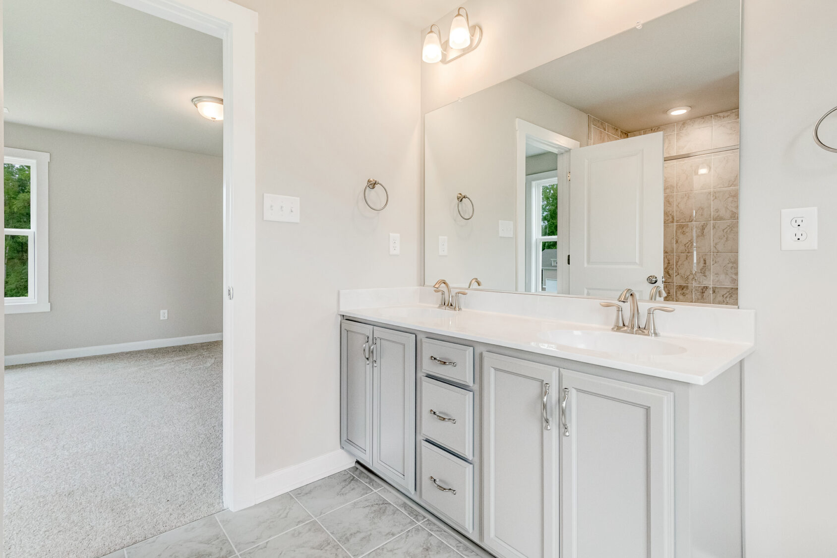 Modern bathroom in Poplar Village with double vanity, large mirror, and view into the carpeted bedroom.