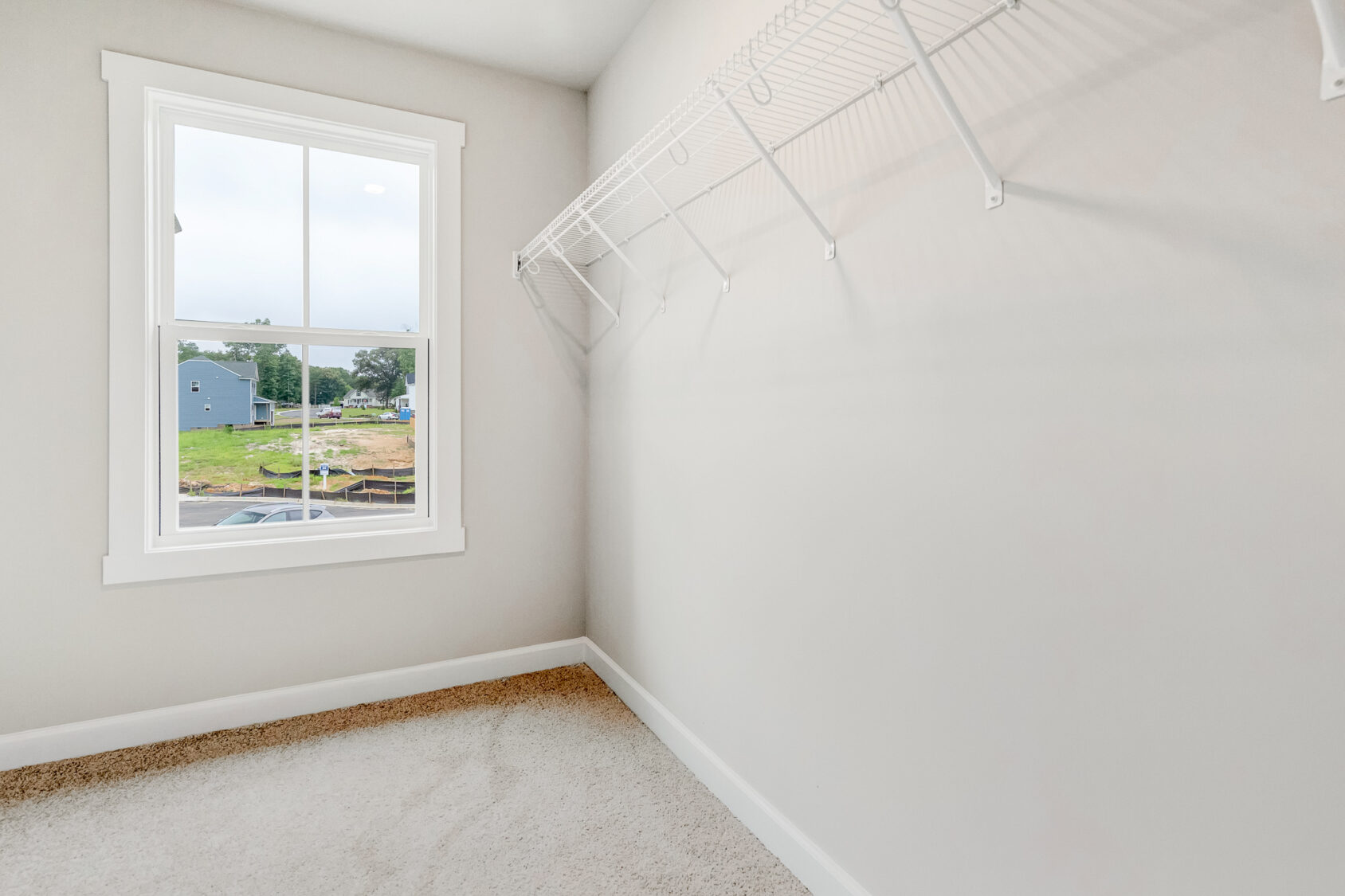 Empty walk-in closet with white wire shelf, beige carpet, and window overlooking Poplar Village in Lot 22.