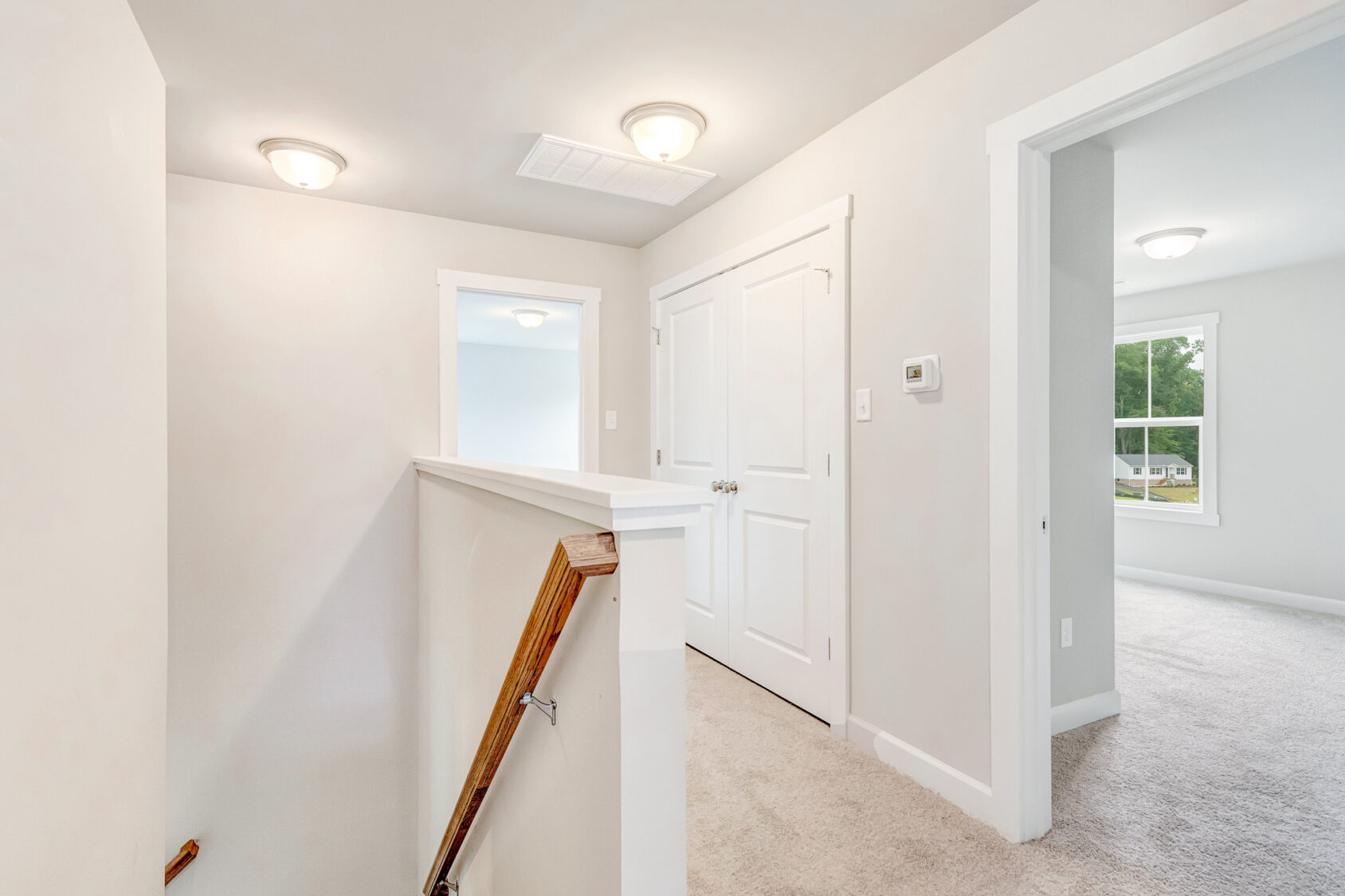 Bright hallway at the top of stairs in Lot 22, Poplar Village, with white doors, beige walls, and carpeted floors.