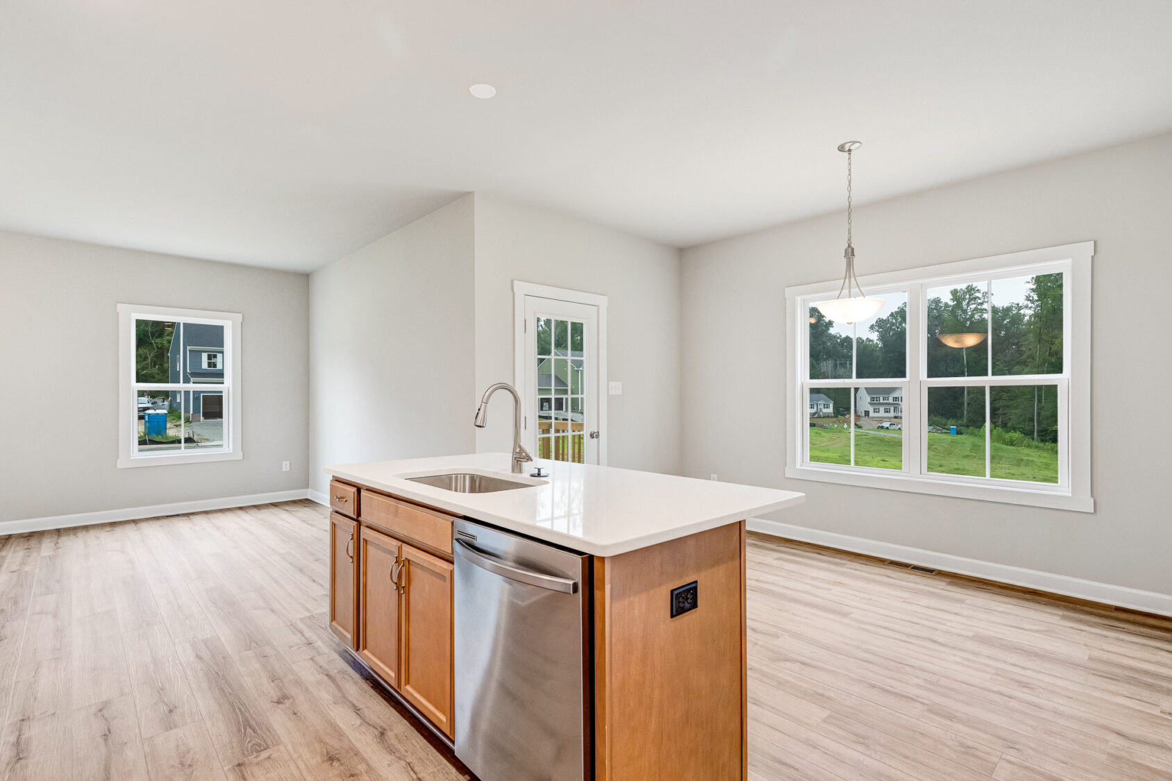 Bright kitchen with wood floors, island sink, and large windows overlooking the green yard in Poplar Village Lot 22.
