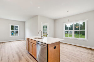 Bright kitchen with wood floors, island sink, and large windows overlooking the green yard in Poplar Village Lot 22.