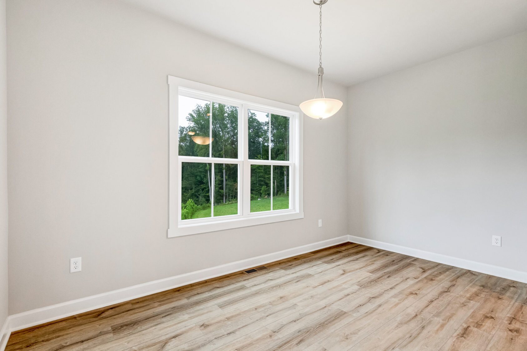 Bright, empty room with wood floors in Poplar Village Lot 22, light gray walls, large window, and ceiling light.