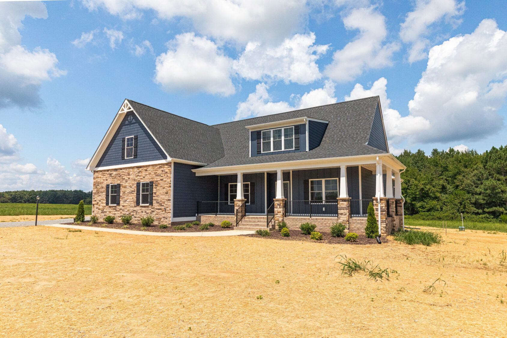 Modern blue house with stone accents and covered porch, surrounded by a dry, grassy landscape under a blue sky.