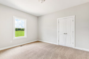 Empty room with beige carpet, light gray walls, a window with a view, and white double closet doors.