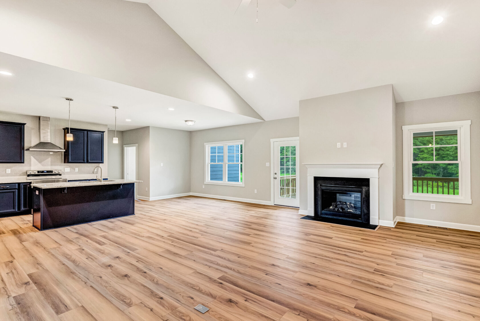 Open-concept living room and kitchen with wood floors, a fireplace, and large windows letting in natural light.