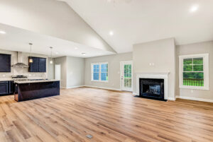 Open-concept living room and kitchen with wood floors, a fireplace, and large windows letting in natural light.