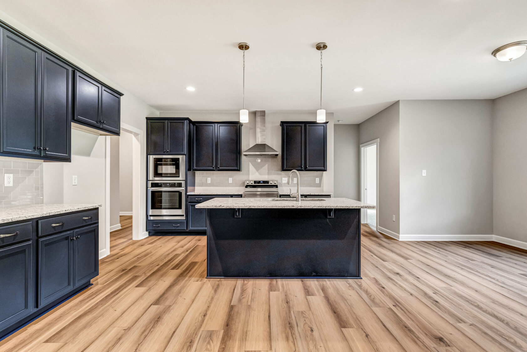 Modern kitchen with dark cabinets, island, pendant lights, stainless appliances, and light wood flooring.