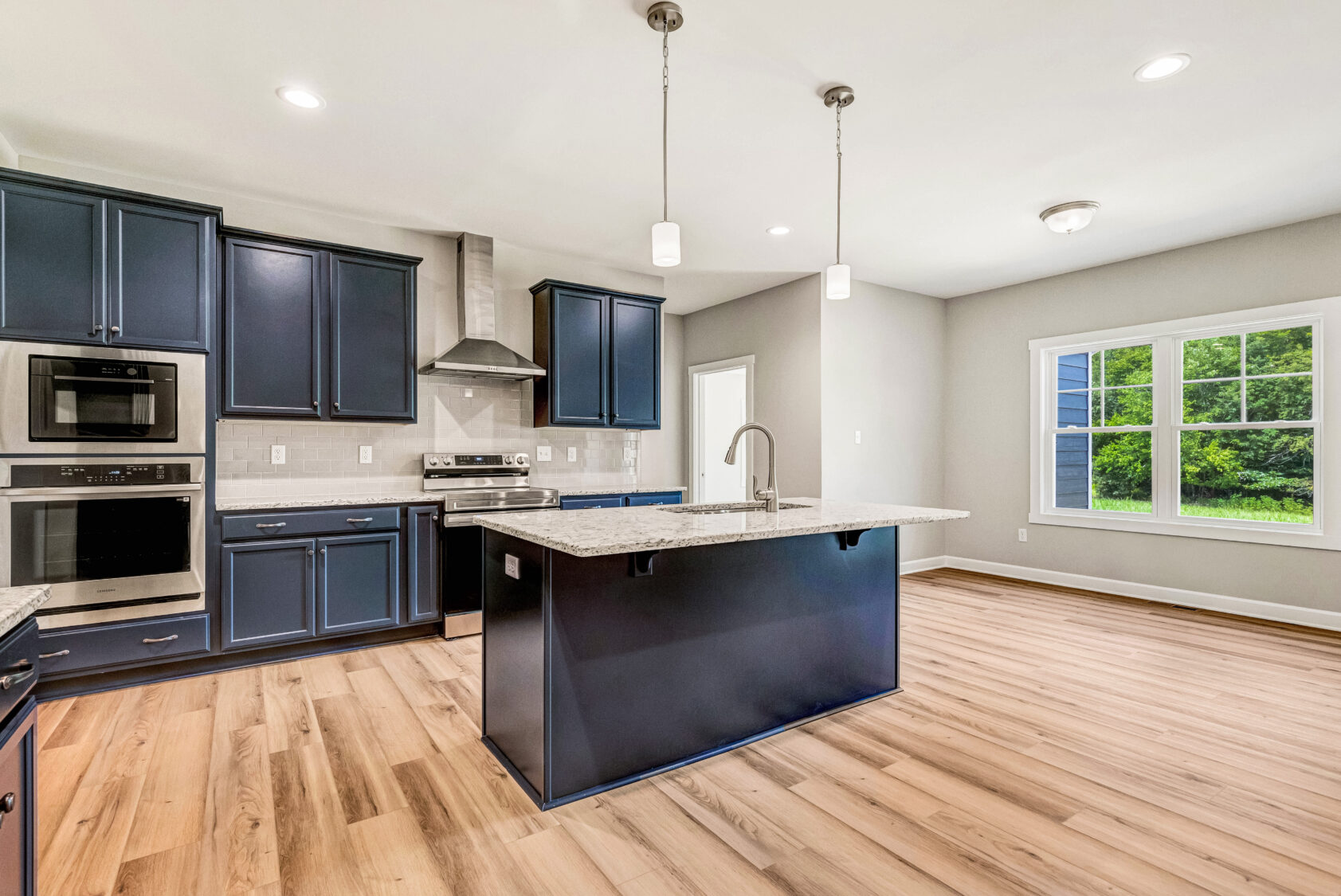 Modern kitchen with navy cabinets, stainless steel appliances, island, and large window overlooking greenery.