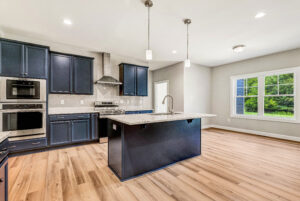 Modern kitchen with navy cabinets, stainless steel appliances, island, and large window overlooking greenery.