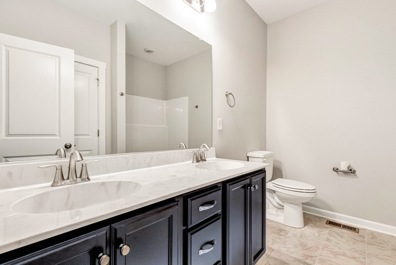 Modern bathroom with double sinks, large mirror, toilet, and light-colored walls and flooring.