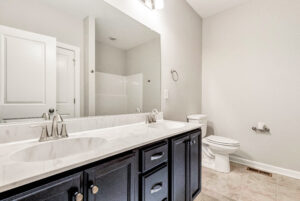 Modern bathroom with double sinks, large mirror, toilet, and light-colored walls and flooring.