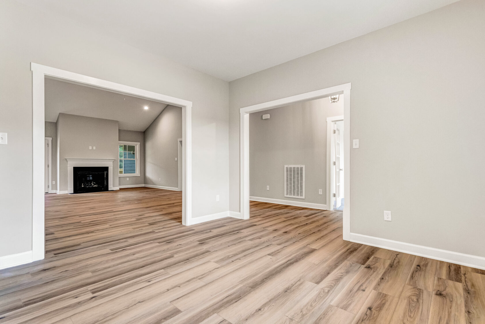 Bright, empty room with light wood floors, beige walls, and wide doorways leading to other rooms.