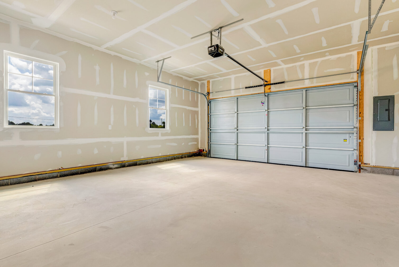 Empty two-car garage with unfinished drywall, two windows, and a closed garage door.