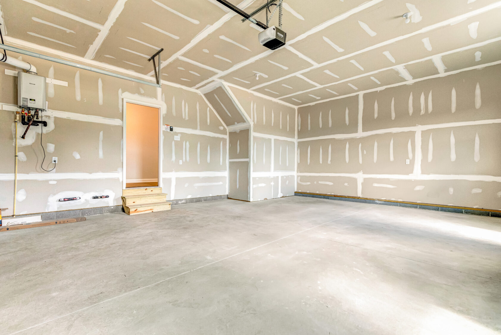 Empty, newly constructed garage with unfinished drywall, concrete floor, and a door with wooden steps.
