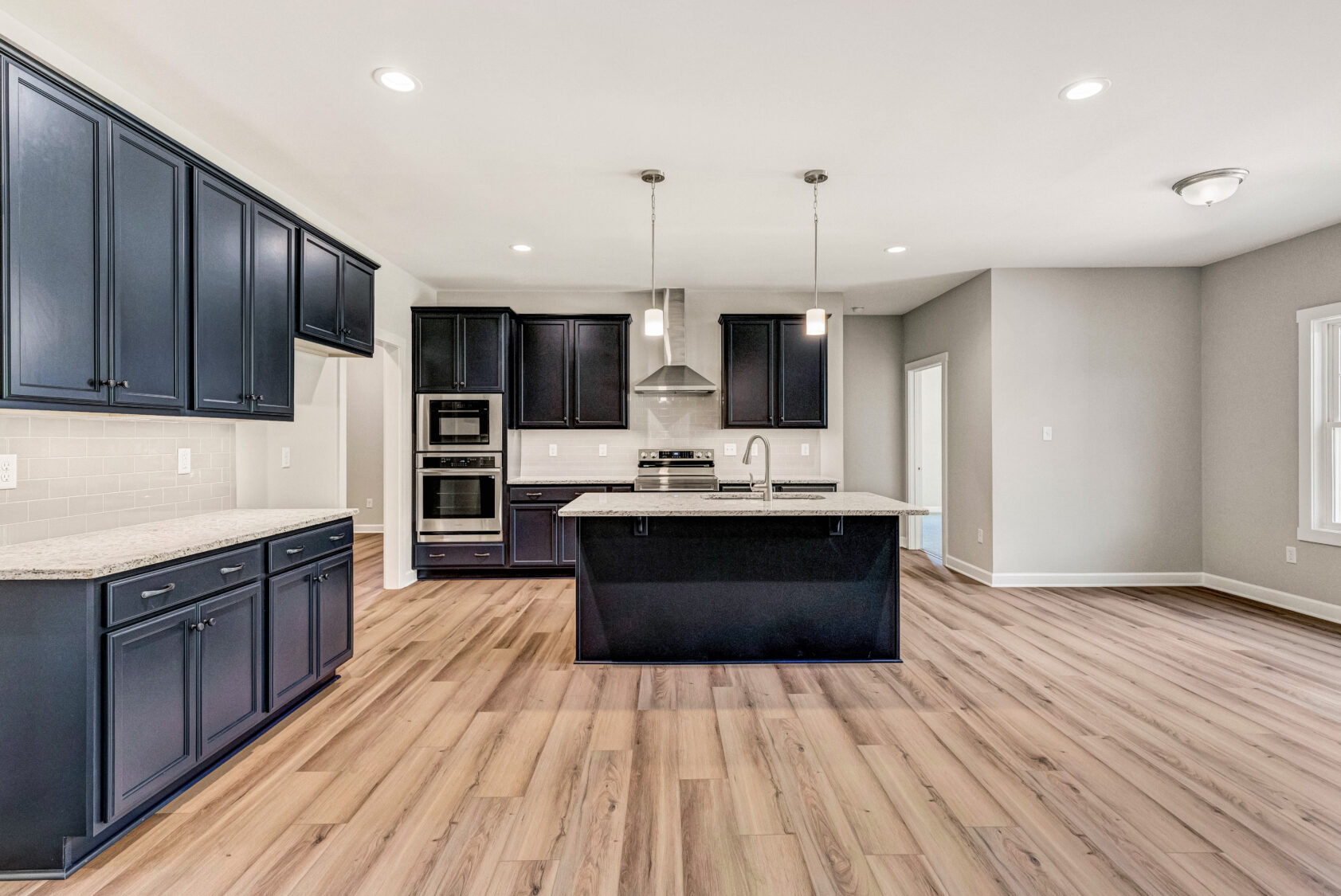 Modern kitchen with navy cabinets, island, stainless steel appliances, and light wood flooring.