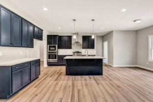 Modern kitchen with navy cabinets, island, stainless steel appliances, and light wood flooring.