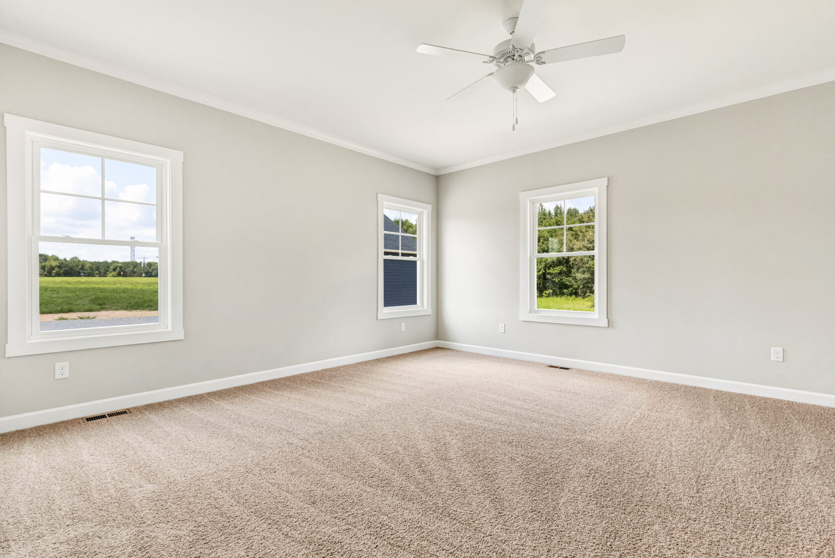 Empty room with beige carpet, light gray walls, three windows, and a ceiling fan.