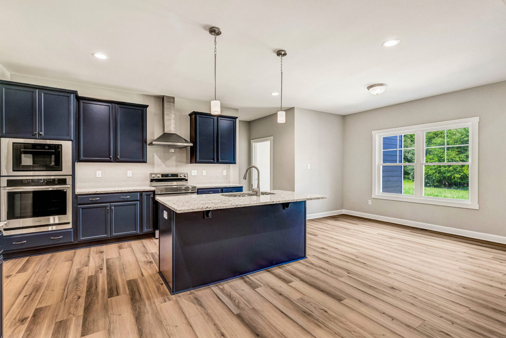 Modern kitchen with navy cabinets, island, stainless appliances, wood flooring, and large window.