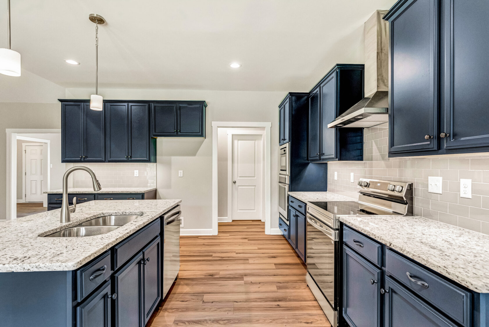Modern kitchen with navy cabinets, granite countertops, stainless steel appliances, and wood flooring.