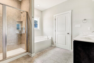 Modern bathroom with a glass shower, white bathtub, vanity, and tile flooring.