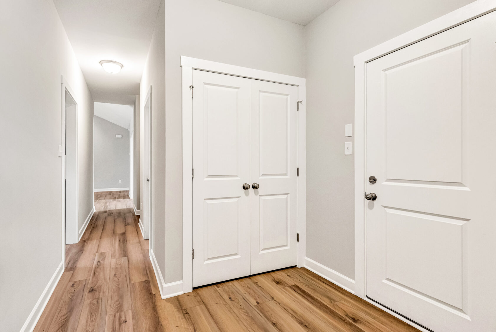 Bright hallway with light wood floors, white doors, and neutral-colored walls in a modern home.