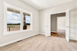Bright empty room with beige carpet, large window, and open French doors leading to a space with wood flooring.