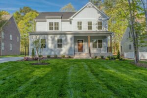 Two-story white house with a porch and well-kept green lawn in the heart of Shirley Commons on a sunny day.