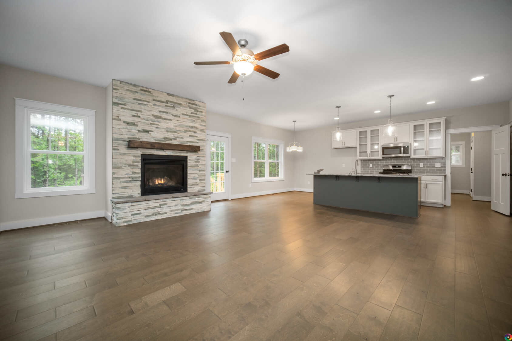 Spacious modern living area at Shirley Commons with fireplace, wood floors, ceiling fans, and open kitchen with island.