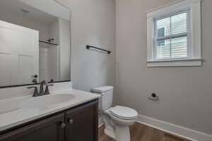 Modern Shirley Commons bathroom with a sink, dark wood vanity, toilet, window, and neutral-toned walls and floor.