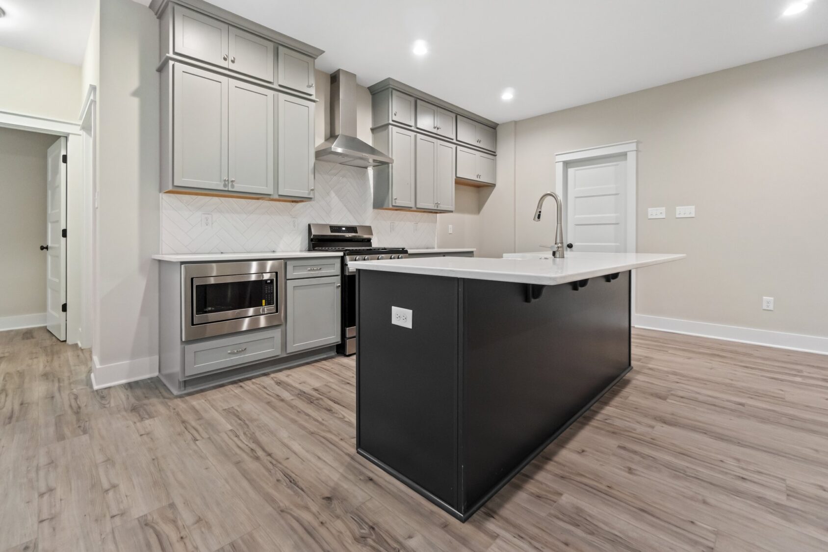Modern kitchen at Shirley Commons with gray cabinets, stainless appliances, white island, and wood flooring.
