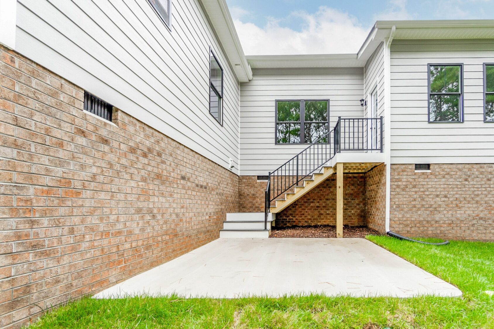 A small concrete patio with stairs leads up to Shirley Commons, a white house with brick siding and grassy lawn.