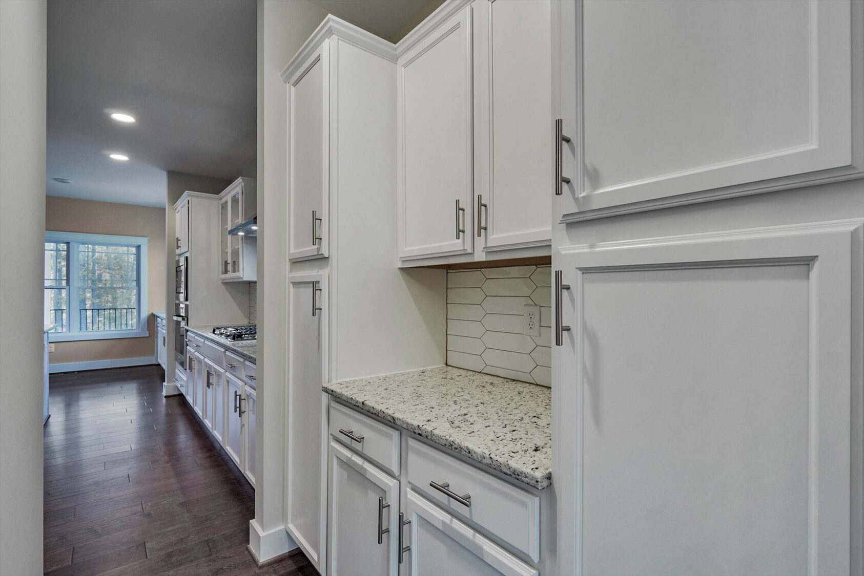 Modern kitchen with white cabinets, granite countertops, and hexagon backsplash in Poplar Village near Albany, sunlit room view.