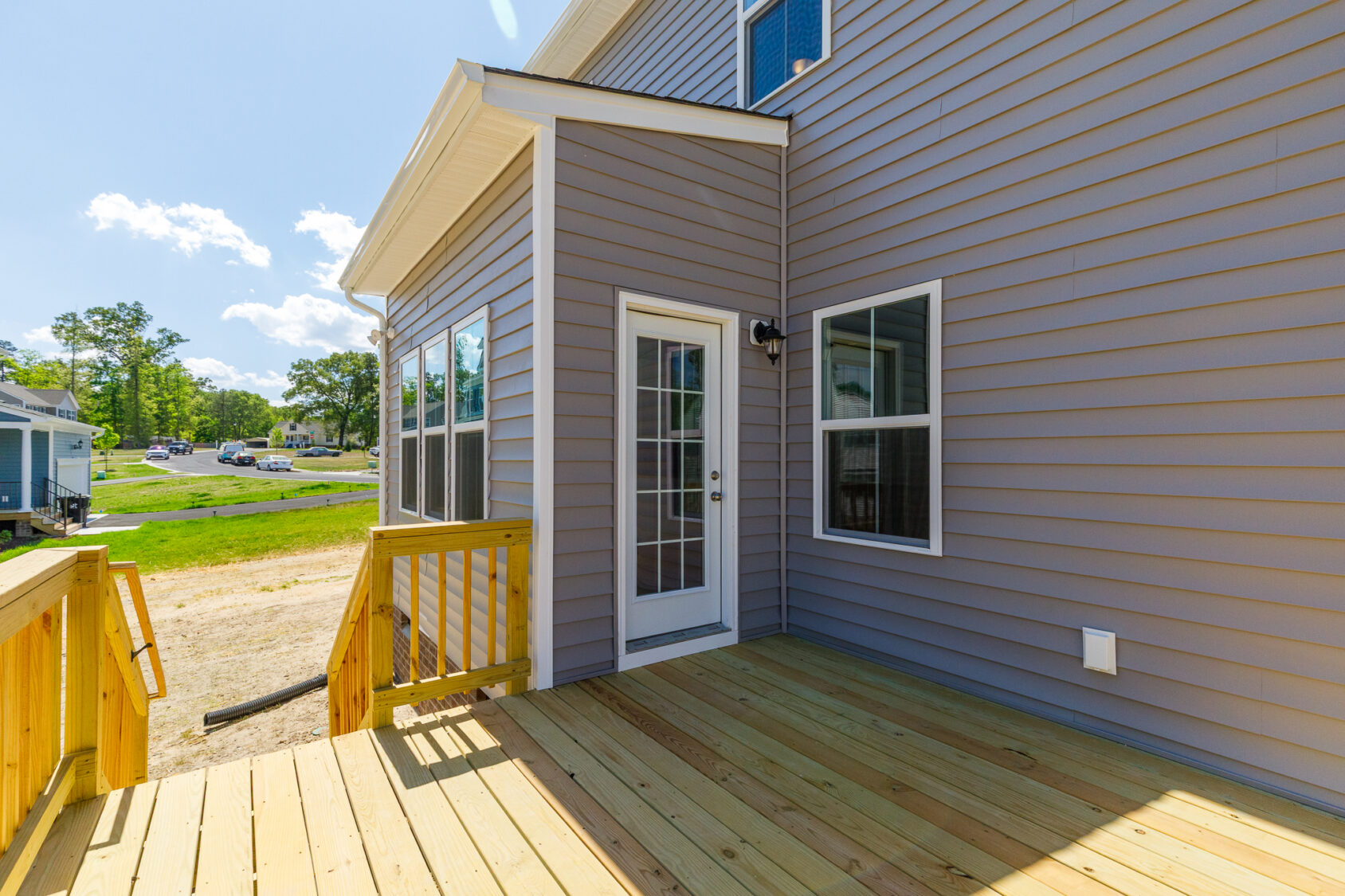 A new wooden deck and steps lead to a white door on a gray home at Lot 28, Poplar Village, on a sunny day.
