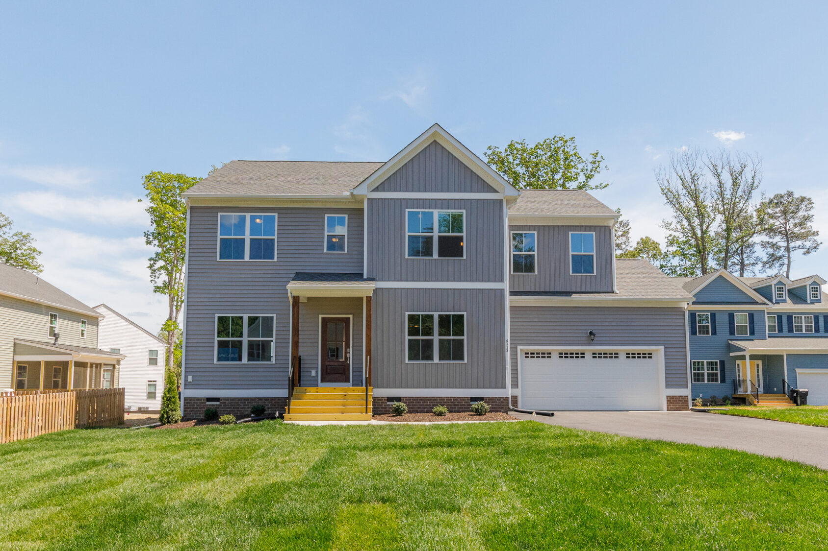 Two-story gray suburban house in Poplar Village with a front porch, garage, driveway, and well-kept green lawn.