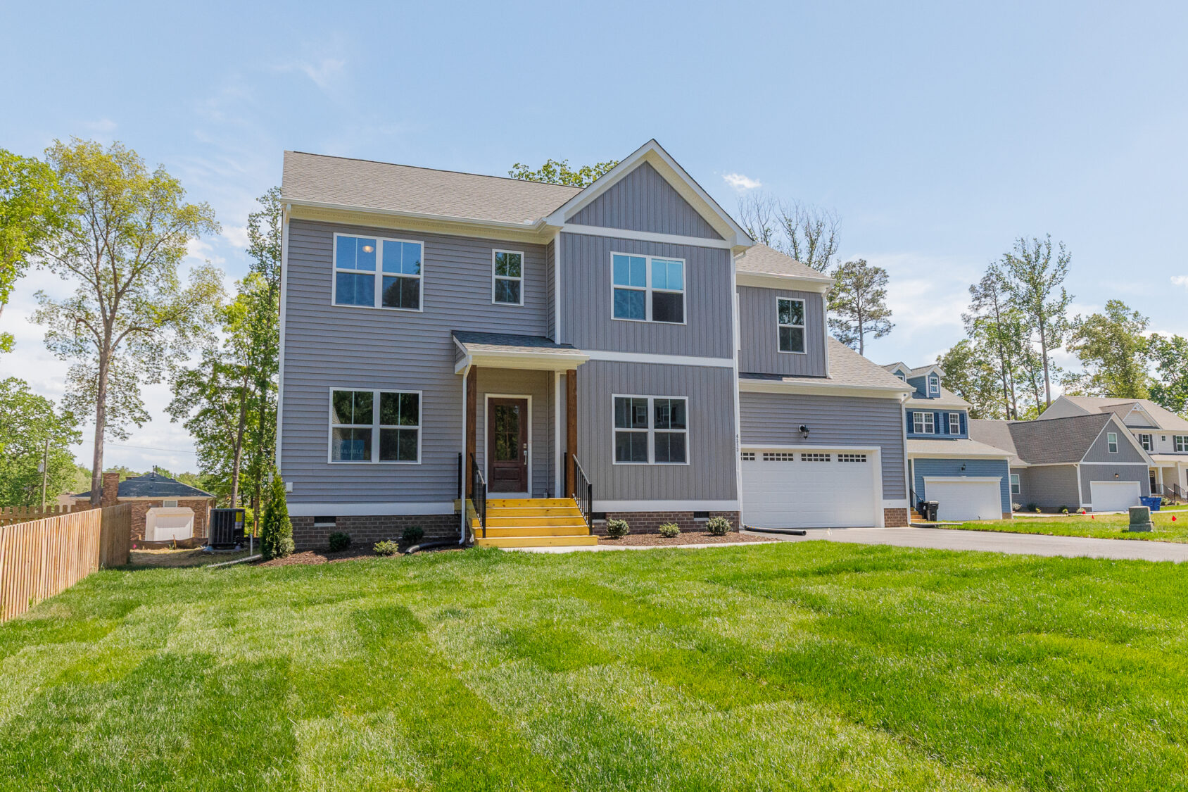 Two-story gray house in Poplar Village with yellow steps, attached garage, and green lawn under a clear blue sky.