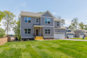 Two-story gray house in Poplar Village with yellow steps, attached garage, and green lawn under a clear blue sky.