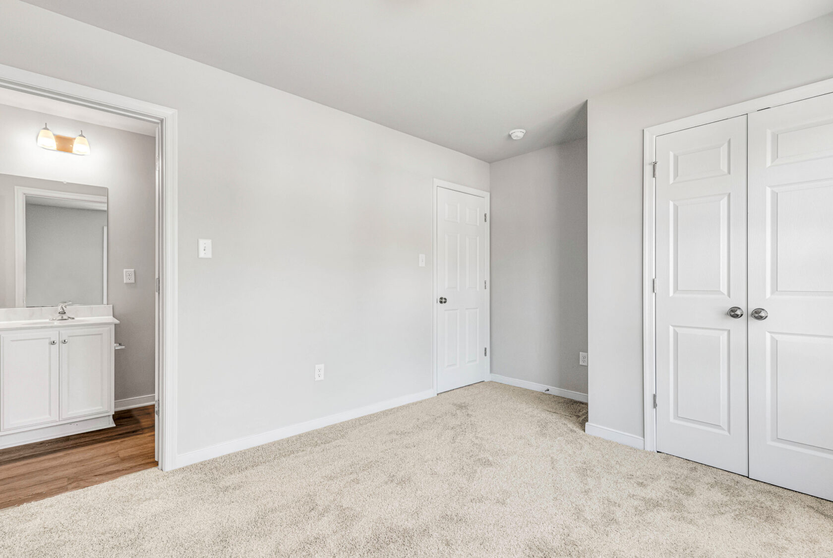 A bright, empty bedroom in Poplar Village with beige carpet, double closets, and a view into a bathroom.