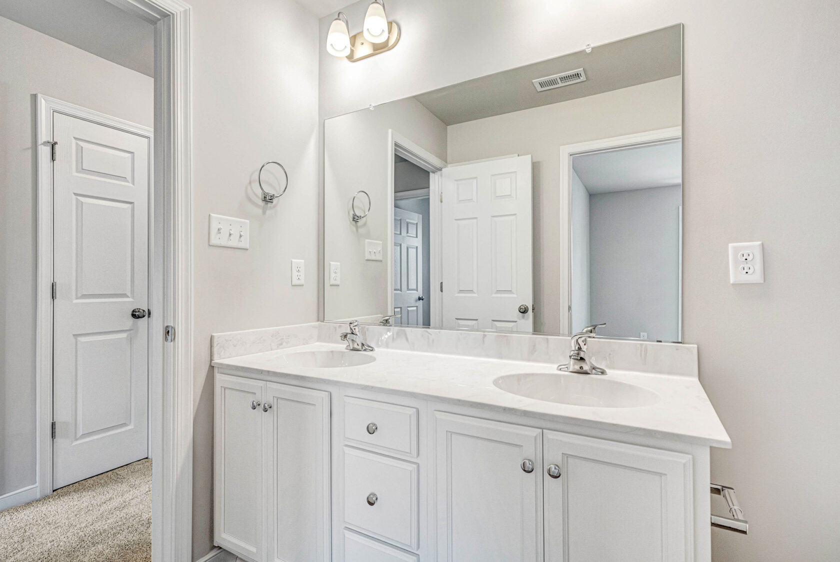 White double-sink bathroom vanity with large mirror in Poplar Village Lot 28, featuring bright overhead lighting.