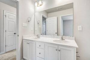 White double-sink bathroom vanity with large mirror in Poplar Village Lot 28, featuring bright overhead lighting.