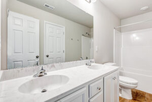 Modern bathroom in Poplar Village, Lot 28, with double sink vanity, large mirror, white cabinets, and shower by the toilet.