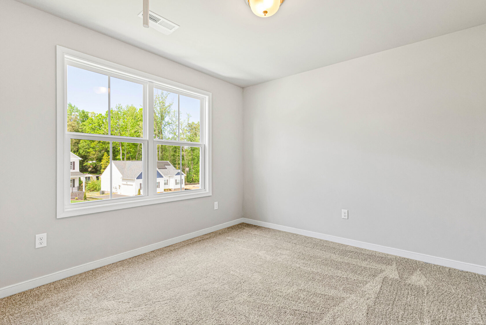 Empty room with beige carpet and gray walls in Poplar Village, featuring a large window with views of Lot 28 and greenery.