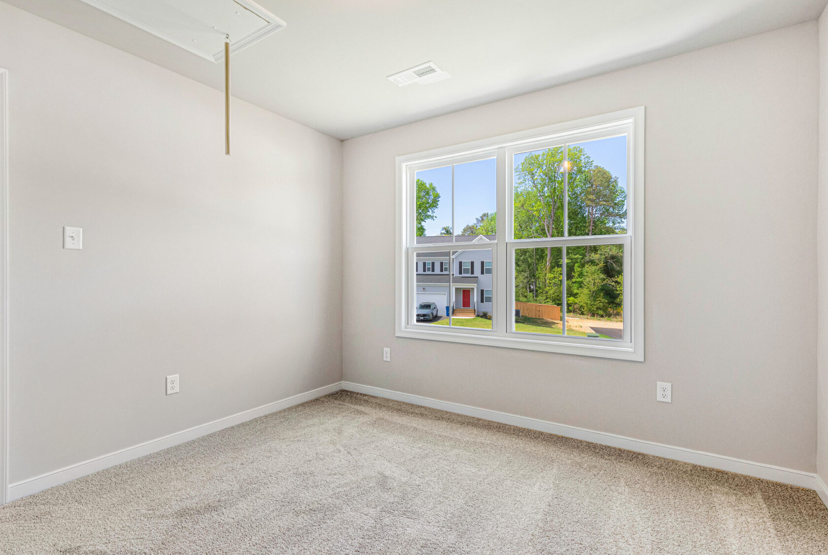 Empty carpeted room with beige walls, ceiling hatch, and large window overlooking Poplar Village from Lot 28.
