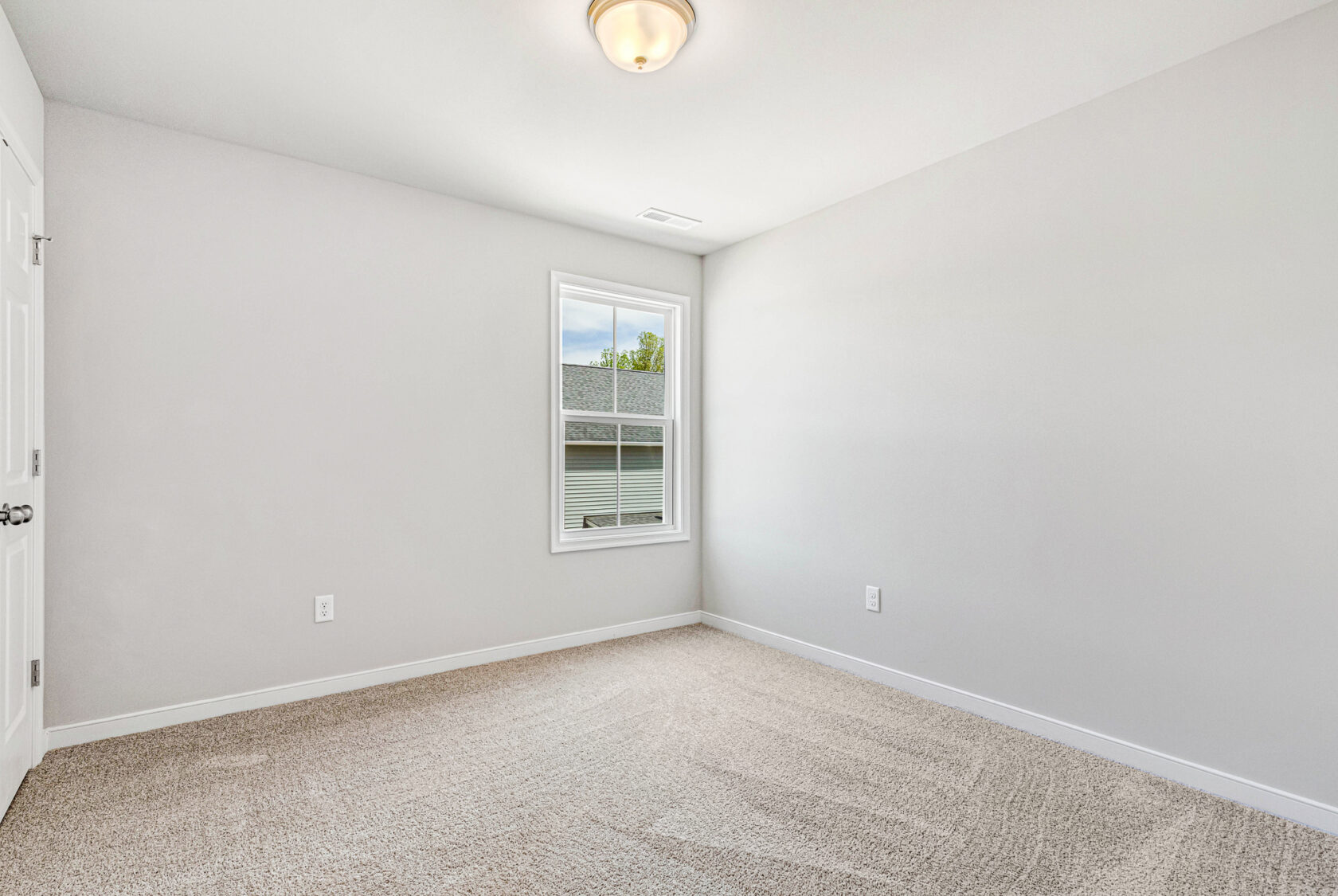 Bright, empty room in Poplar Village Lot 28 with beige carpet, white walls, window, and ceiling light fixture.
