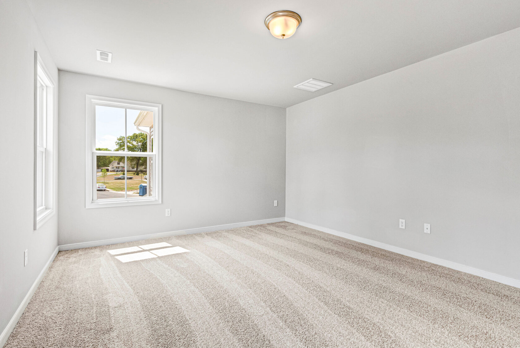 Empty room in Poplar Village, Lot 28, with light gray walls, two windows, ceiling light, and beige carpet flooring.
