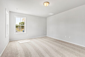 Empty room in Poplar Village, Lot 28, with light gray walls, two windows, ceiling light, and beige carpet flooring.