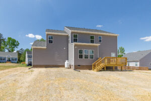 Two-story gray house on Lot 28 with a wooden deck in Poplar Village under a clear blue sky.