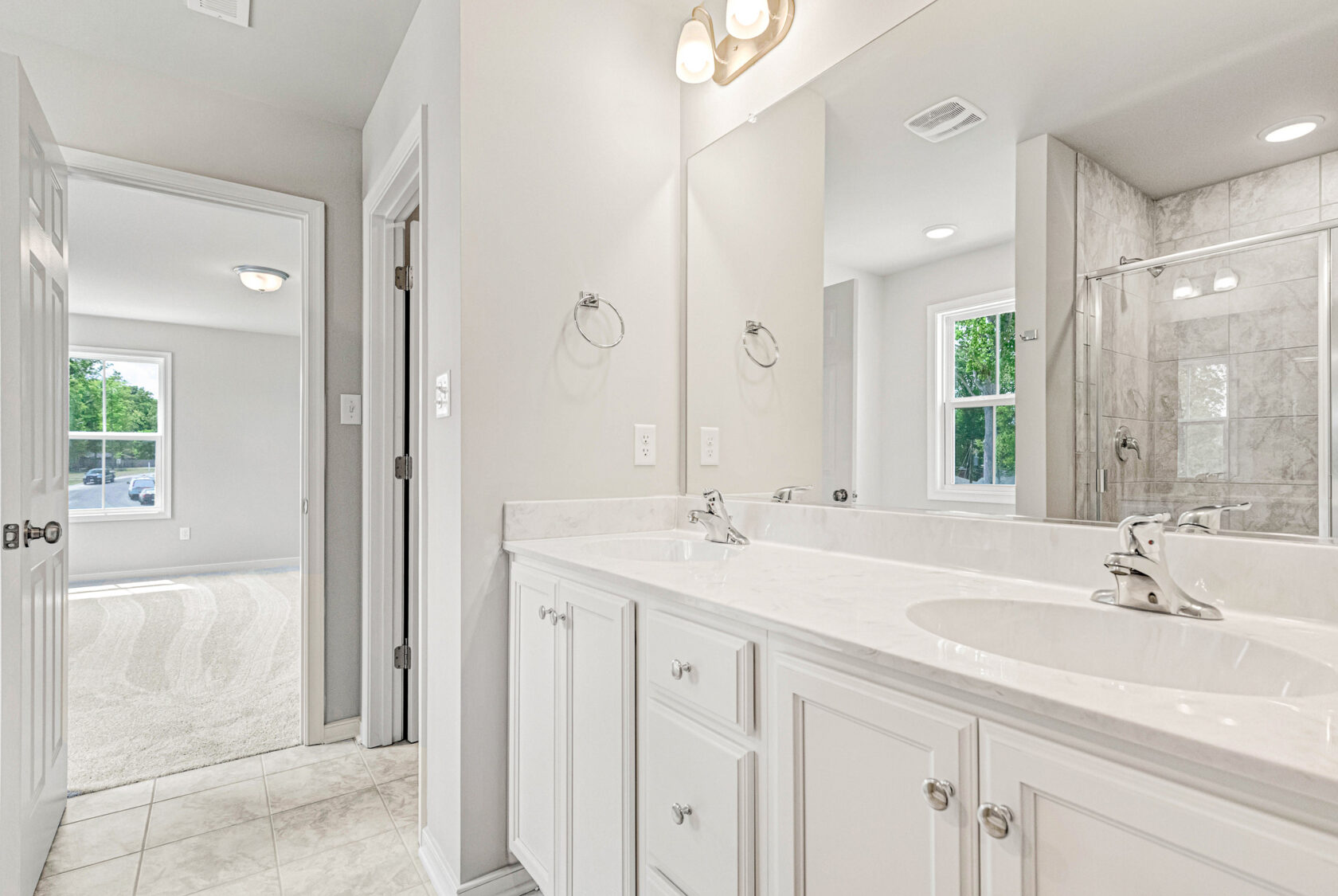 Modern bathroom with double sink vanity, large mirror, and view into Lot 28 of Poplar Village’s bright carpeted bedroom.