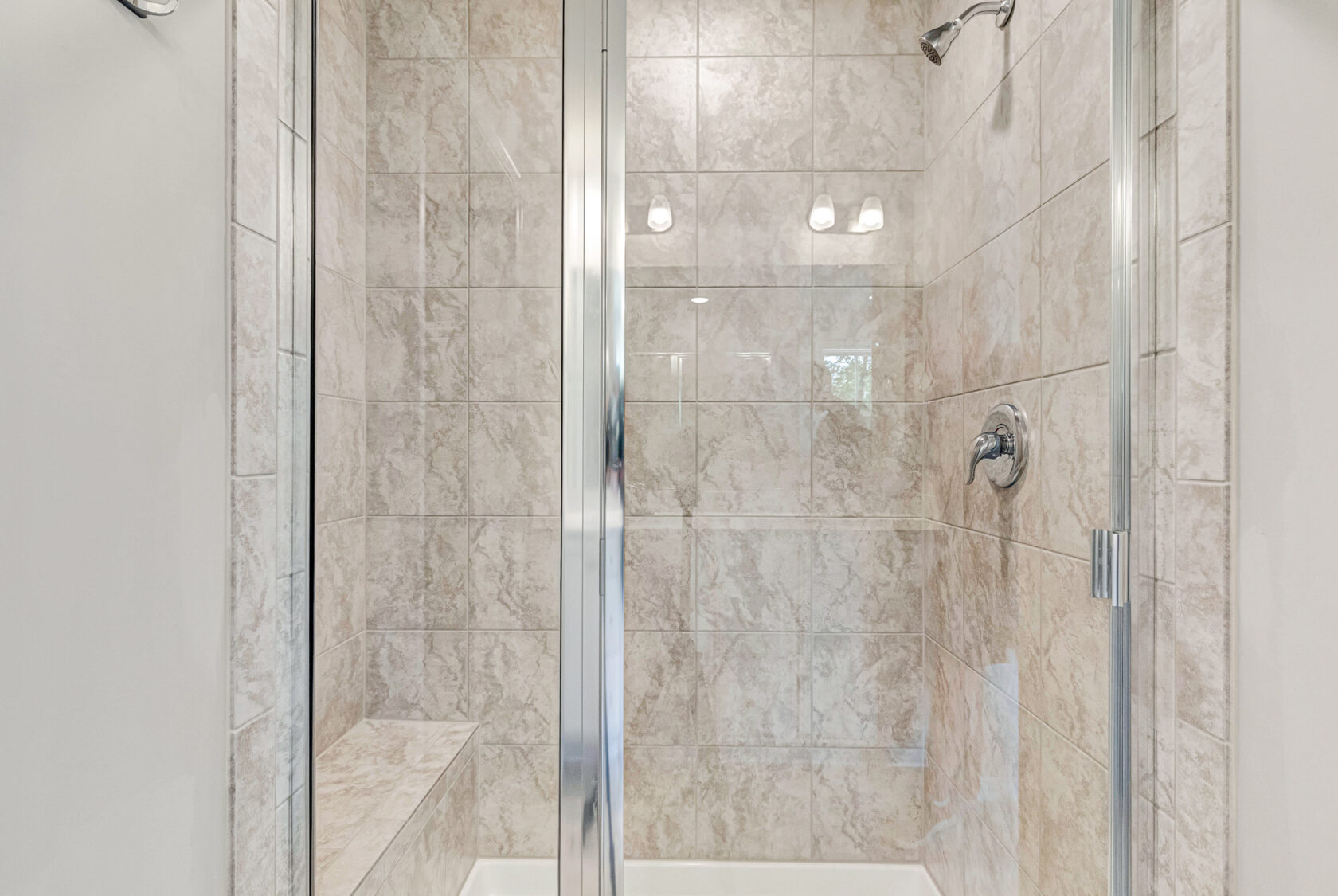 Glass shower with beige tile walls, built-in bench, and metal fixtures in Poplar Village Lot 28.