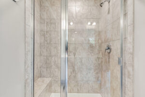 Glass shower with beige tile walls, built-in bench, and metal fixtures in Poplar Village Lot 28.