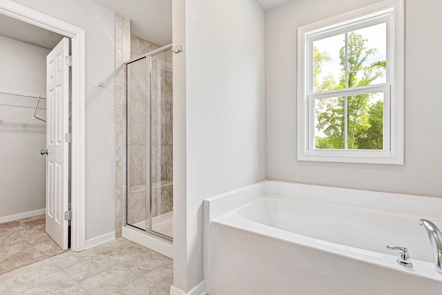 Bright bathroom in Lot 28, Poplar Village with a large tub, glass shower, closet door, and window with tree views.
